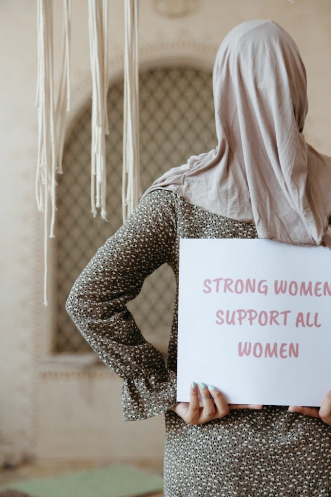 A woman in a hijab holds a sign with an empowering message about women's support.